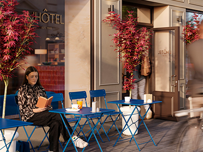 Una mujer sentada en una mesa plegable azul en la terraza de una cafetería leyendo un libro frente a un edificio llamado "L'HÔTEL", flanqueada por arces japoneses en macetas.