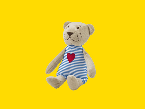 Oso de peluche FABLER BJÖRN con traje a rayas azules y corazón rojo sobre fondo amarillo.