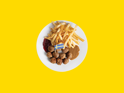White plate with Swedish meatballs and French fries on a yellow background.