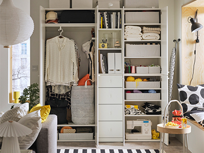 Open white modular wardrobe organizing clothes, books, storage boxes, and a sewing machine.