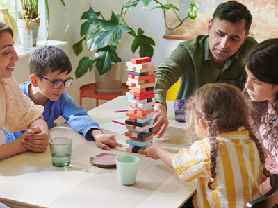 Family playing with a colorful block tower at a dining table.