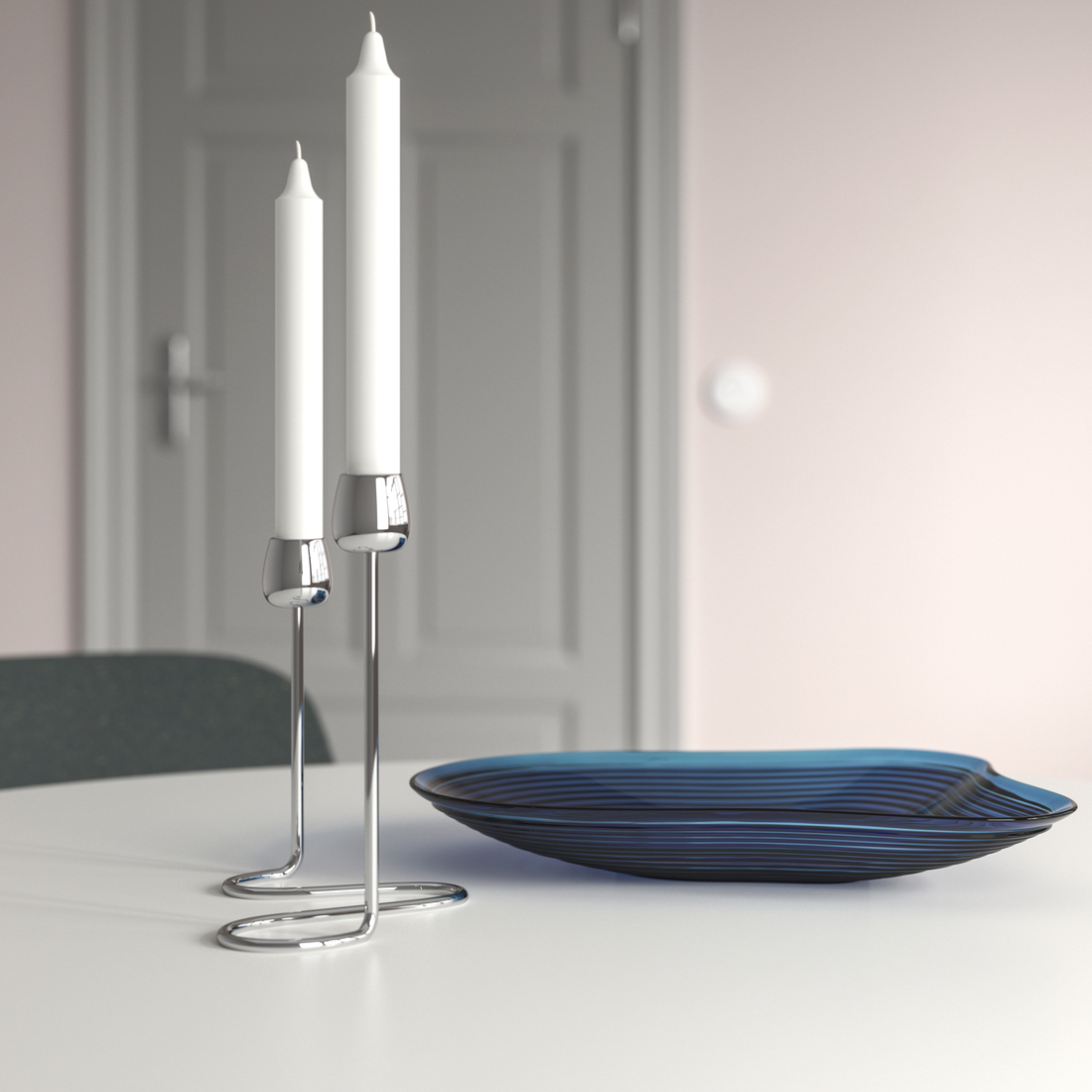 Two white taper candles in wavy chrome metal candle holders next to a blue glass bowl on a white table.