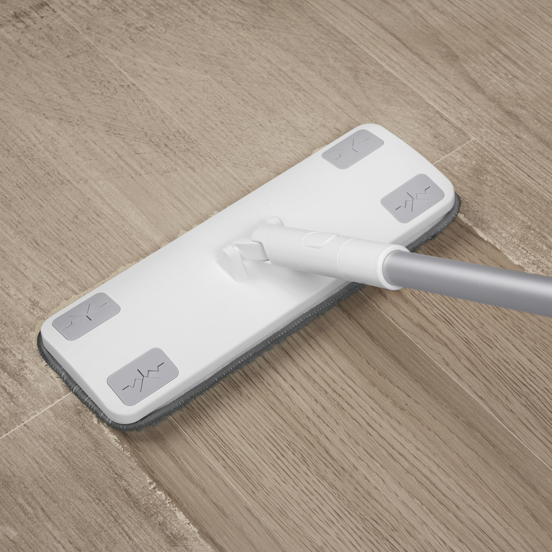 White flat cleaning mop with a gray microfiber pad sliding on a light wood floor.