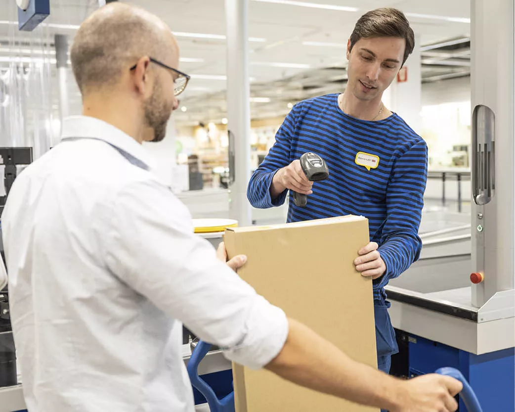 Cashier scanning a large cardboard box held by a customer at a store checkout.