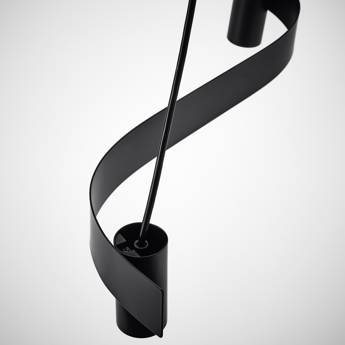 Plano detalle de una lámpara colgante moderna de metal negro con una tira curva en forma de 'S' sobre un fondo claro.