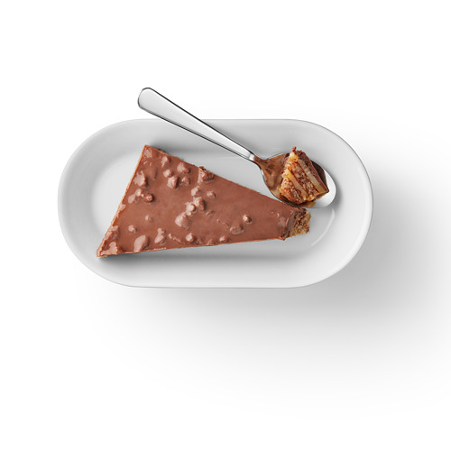 Rebanada de bizcocho en capas con crujiente de almendras y chocolate en plato blanco.