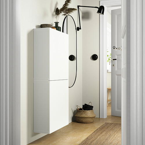 White BESTÅ storage unit with two doors. Mounted on wall, complemented by woven basket and wall lamp. Tall, narrow design.