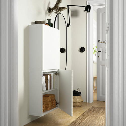 A modern hallway a white BESTÅ wall cabinet with adjustable shelves, books, and a wicker basket. A wall-mounted light adds functionality.