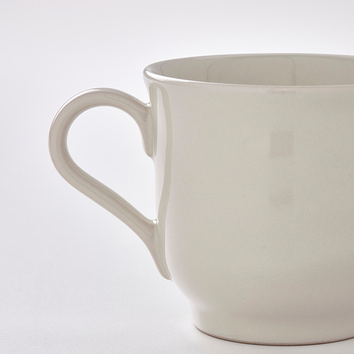 Primer plano de una taza lisa de color crema con un mango grande y ergonómico. La taza parece robusta y bien elaborada, mostrando una sensación rústica y hecha a mano.
