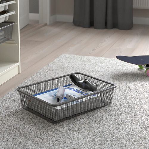 Cesta de almacenamiento de malla sobre alfombra, con soporte para control remoto y libro, parte de la serie TROFAST.