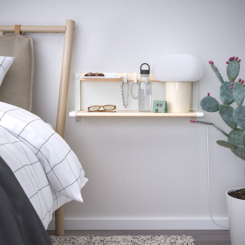 Estante de pared de madera clara con ganchos, botella de agua, vasos y joyas cerca de la cama.