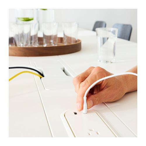 La mano conecta el cable blanco con el enchufe a una mesa alta elegante y moderna con gestión de cables.