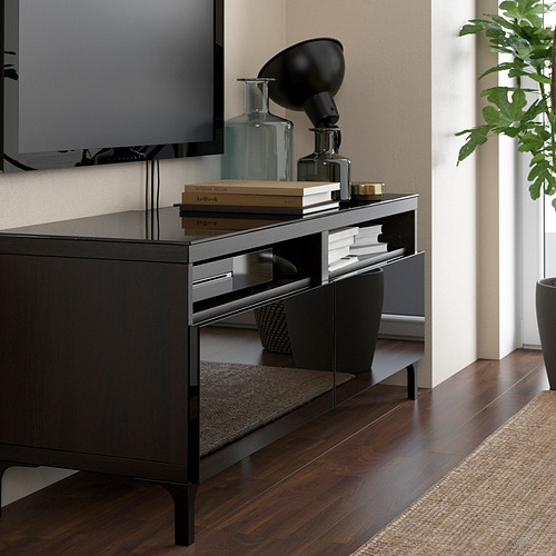 Mueble de vidrio para tv con libros, jarrones, lámpara, tv, planta, alfombra sobre pisos de madera.