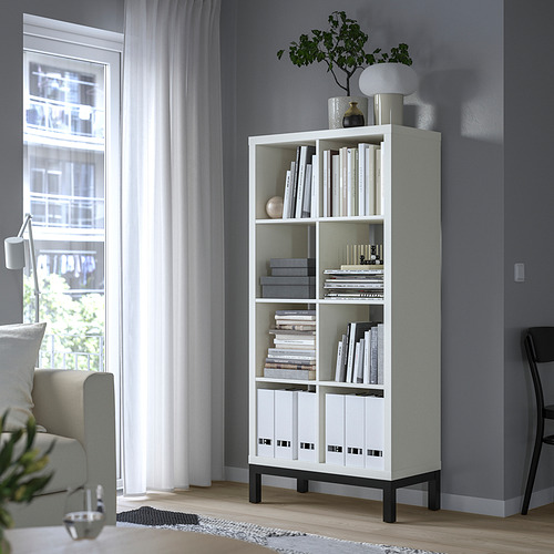 Estantería blanca KALLAX con libros y decoración cerca de una ventana, que ofrece un almacenamiento moderno y minimalista.