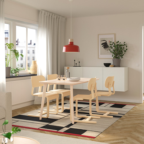 Moderno juego de comedor con mesa de madera, 4 sillas LYCKAN, lámpara colgante roja, plantas y una alfombra con estampados. Espacio luminoso y aireado.