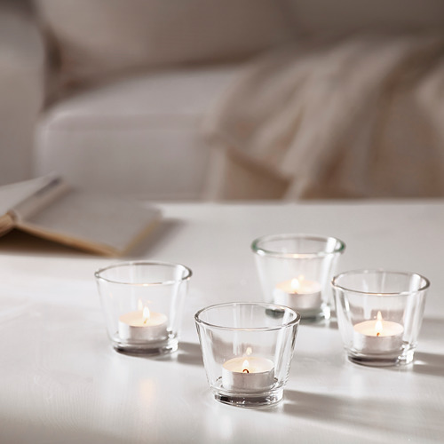 Cuatro pequeñas velas encendidas en soportes de vidrio transparente sobre una mesa, creando un ambiente cálido y acogedor.