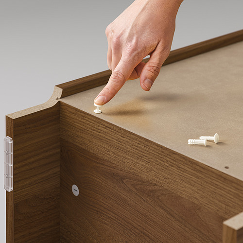 Una persona monta una estantería BILLY, utilizando un panel de madera y bisagras blancas.