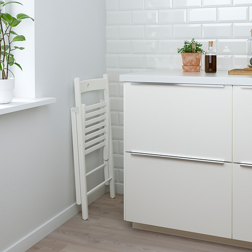 Cocina limpia con gabinete blanco, cajón y silla con respaldo de escalera contra la pared; plantas y botella en el mostrador.