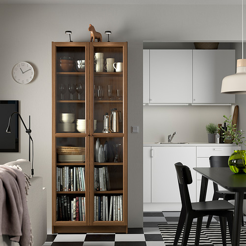 Librería BILLY con puertas de vidrio, llena de artículos, entre un comedor y la cocina en una casa moderna.