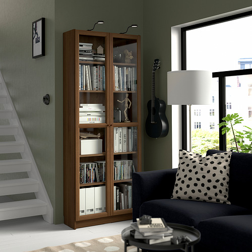 Sala de estar moderna con librería Billy, sofá azul marino y guitarra. Las estanterías contienen libros y decoración. Escalera blanca y gran ventanal.