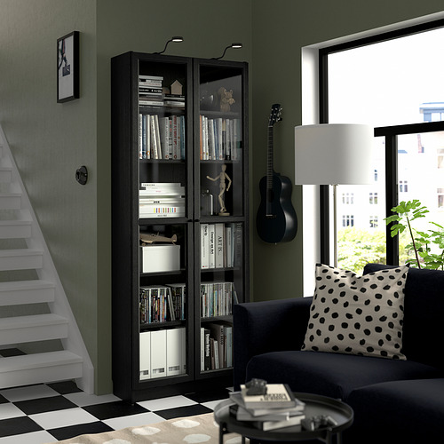 Sala de estar moderna con estantería oscura BILLY, sofá, guitarra, mesa auxiliar y lámpara. Pared verde, piso a cuadros y vista a la ventana.