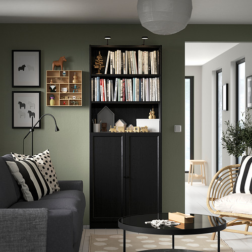 Sala de estar moderna con sofá gris, estantería BILLY negra llena de libros, artículos decorativos y estampados en la pared verde oliva.