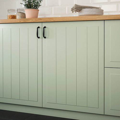 Kitchen cabinets with light green, grooved panel doors. They have dark handles and a wooden countertop with a plant, jars, and plates.