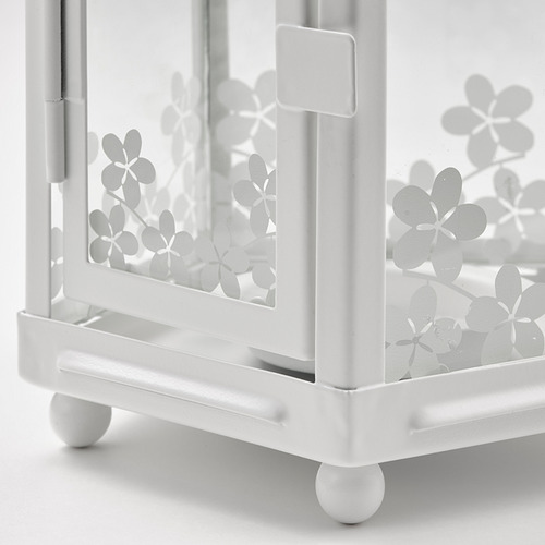 Carro de metal blanco con recortes florales, cuatro ruedas redondas; parte de una línea de productos decorativos.