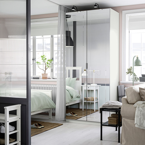 Dormitorio moderno con puerta de espejo, cama reflectante y habitación, creando una sensación de amplitud. La puerta blanca complementa la decoración ligera con cama verde y sofá beige.