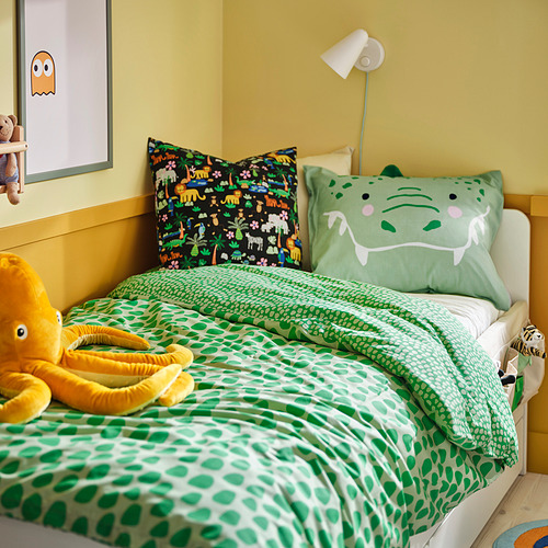 Cama infantil de temática selvática con edredón verde/blanco, pulpo de juguete, lámpara de pared, cuadro.