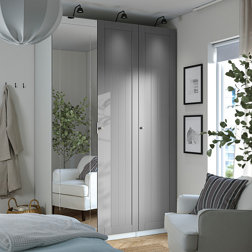 Minimalist bedroom with white PAX wardrobe, mirror door, light wood interiors. White armchair by bed with blue/white bedding, city view window.