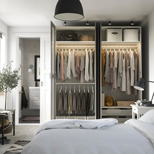 Open wardrobe displaying clothes and accessories, part of a modern bedroom with a bed and lamp.