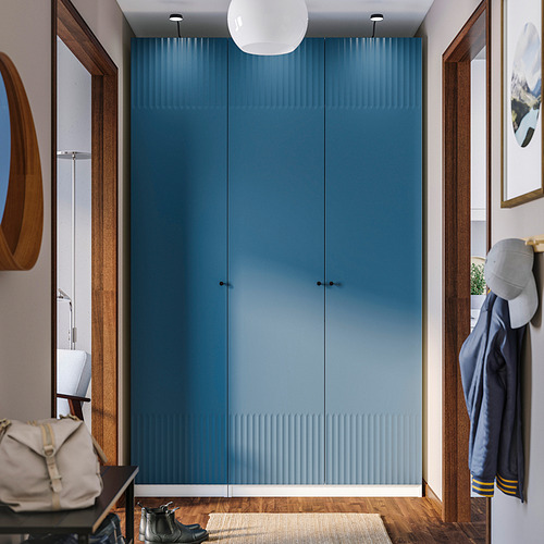 This image shows a blue PAX wardrobe in a room, taller than a nearby coat and hat stand, with wooden accents and a white pendant light above it.