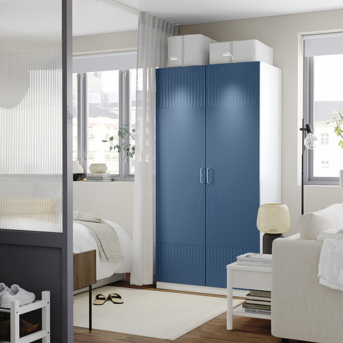 Dormitorio moderno con gran armario azul PAX, detalles en blanco, puertas de cierre suave.
