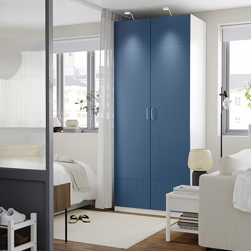 Modern bedroom with blue PAX wardrobe, large window, white rug, and minimalist decor.