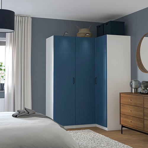 Dormitorio moderno con armario azul y blanco, arcón de madera, espejo redondo y una cama con ropa de cama blanca.
