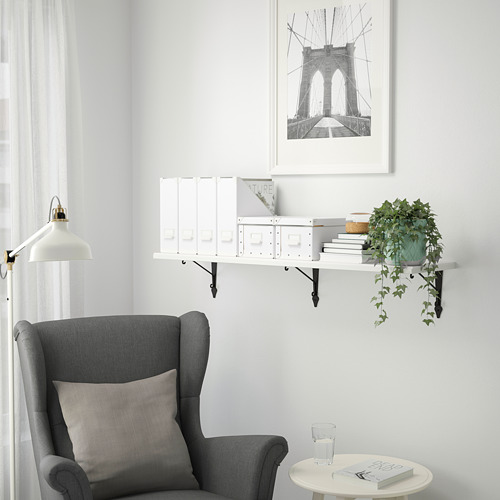 Acogedor rincón con estantería TREHULT, libros, planta y sillón. Estampado del puente de Brooklyn en la parte superior, decoración minimalista.