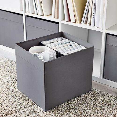 Cubo de almacenamiento gris con divisores que contienen auriculares y DVDs, parte de una estantería KALLAX .