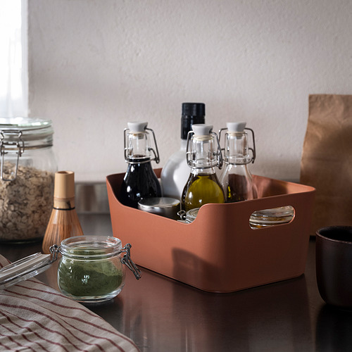 Caja de plástico reciclado naranja con asas que sostienen botellas de vidrio en la encimera de la cocina.