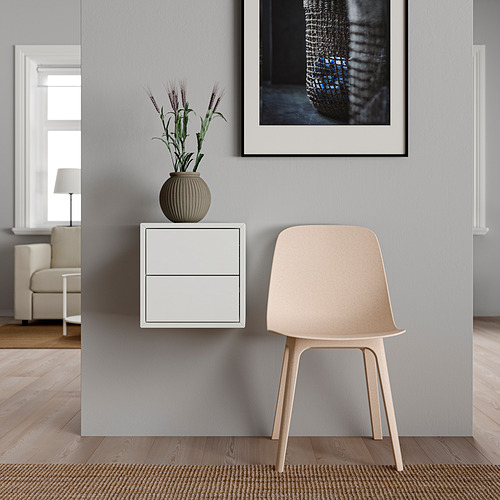 Mueble de almacenaje minimalista EKET blanco con dos cajones, con una silla beige y una planta en maceta en la parte superior. Pared gris con arte enmarcado. Suelo de madera clara.