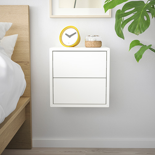 Mueble EKET blanco con 2 cajones, reloj amarillo, cama de madera, hoja de planta verde, dormitorio minimalista.