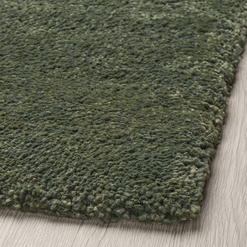 Alfombra verde gruesa y suave sobre suelo de madera, que muestra una textura y artesanía de alta calidad.