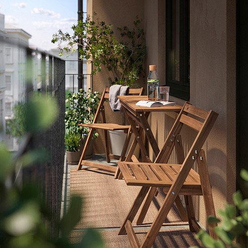 Pequeño balcón con mesa y sillas de madera, plantas verdes y vista a la ciudad.