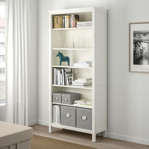 Estantería KVARNVIK blanca bajo la ventana, con libros, cajas y decoración.
