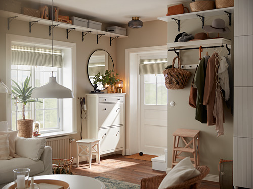 Sala de estar moderna con paredes beige, muebles blancos y decoración de madera. BERGSHULT estanterías, sofá, taburetes, perchero.