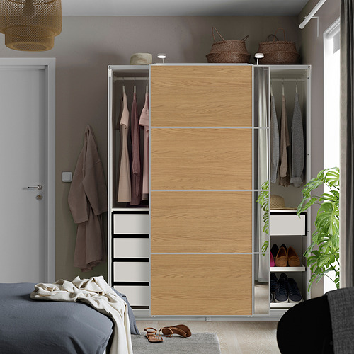 Dormitorio moderno con armario PAX de madera clara, puertas correderas, sección de espejo, ropa y cajones, junto a la cama.