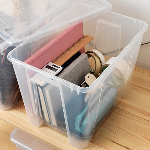 Caja de almacenamiento de plástico transparente con tapa, que contiene útiles escolares como reglas, calculadoras y cuadernos. La tapa tiene una función de bloqueo de clic incorporada.