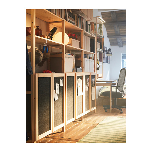 Oficina en casa con estantes de pino IVAR, papeles, libros y una silla de escritorio negra. Los estantes tienen puertas de fieltro con notas clavadas.