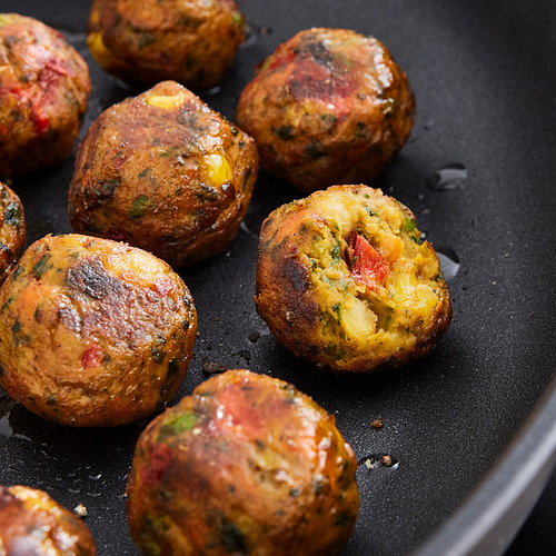 Albóndigas de verduras doradas fritas en una sartén negra.