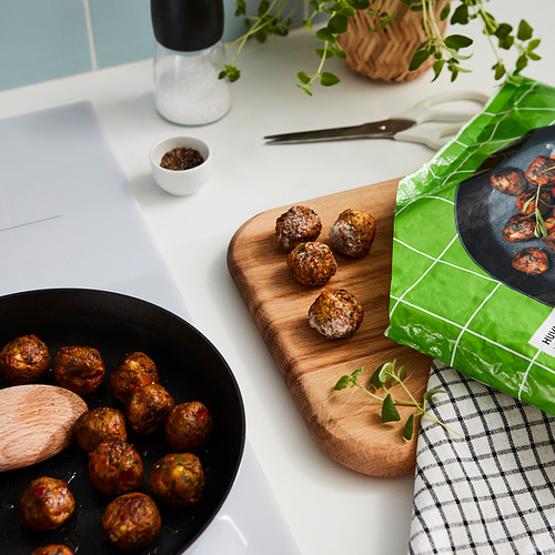 Albóndigas cocidas en sartén, tabla de madera, empaque dice HUVUDROLL con color verde, hierbas, salero y tazón blanco en la encimera de la cocina.